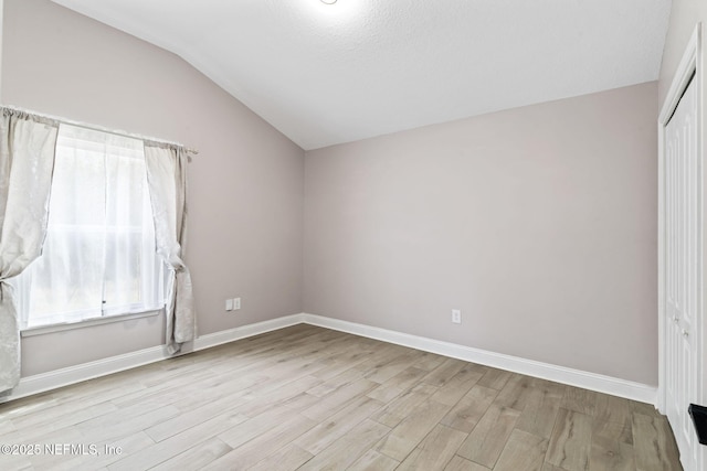 unfurnished room with lofted ceiling, light wood-type flooring, and baseboards