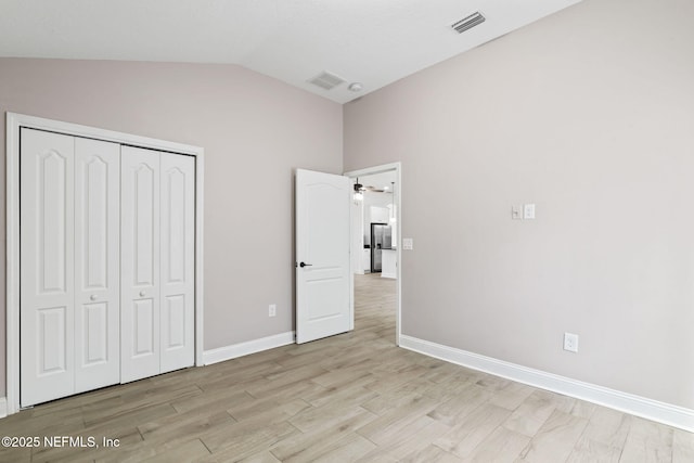 unfurnished bedroom featuring baseboards, visible vents, light wood-style flooring, vaulted ceiling, and a closet