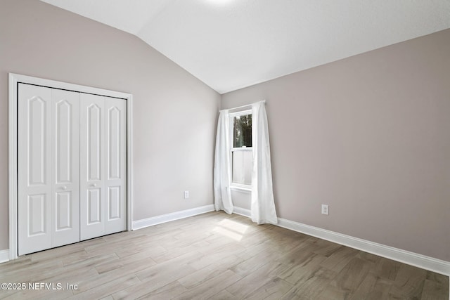 unfurnished bedroom featuring vaulted ceiling, a closet, baseboards, and light wood-style floors