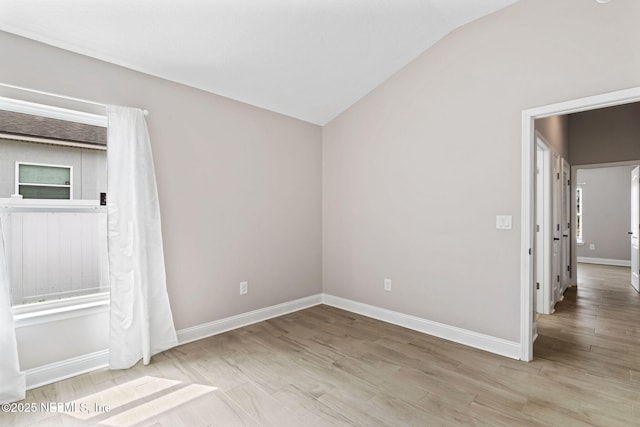 unfurnished room featuring lofted ceiling, baseboards, and wood finished floors