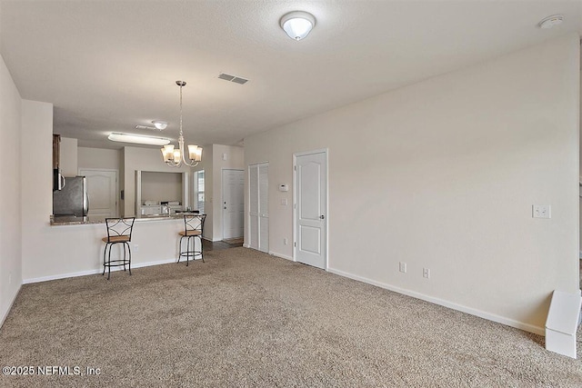 kitchen with a peninsula, a breakfast bar, visible vents, freestanding refrigerator, and carpet