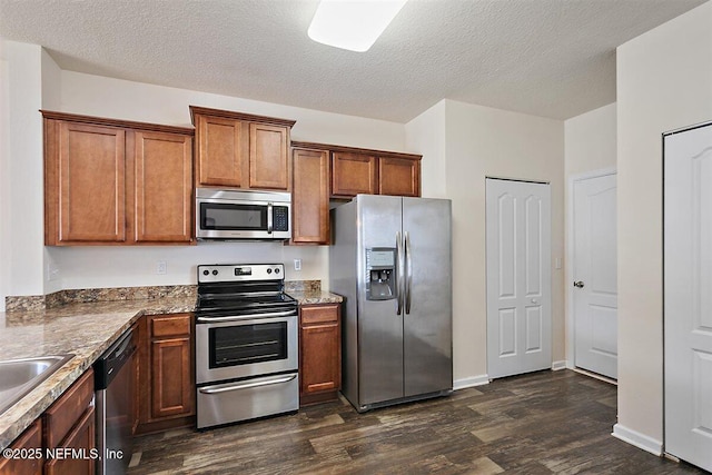 kitchen with stainless steel appliances, dark wood-style flooring, brown cabinetry, and a textured ceiling