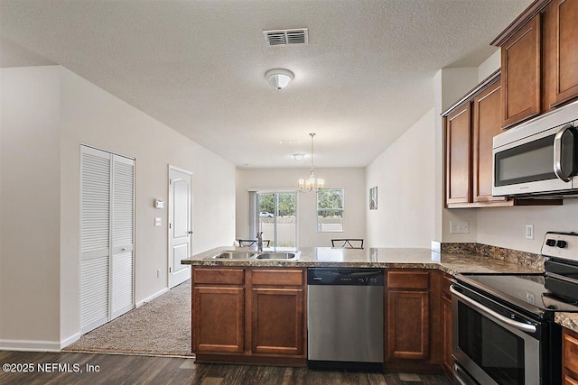 kitchen featuring visible vents, a peninsula, stainless steel appliances, a chandelier, and a sink