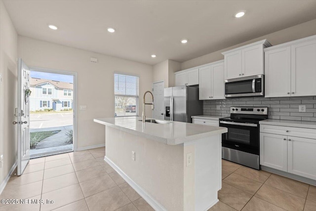 kitchen with stainless steel appliances, a kitchen island with sink, a sink, and tasteful backsplash