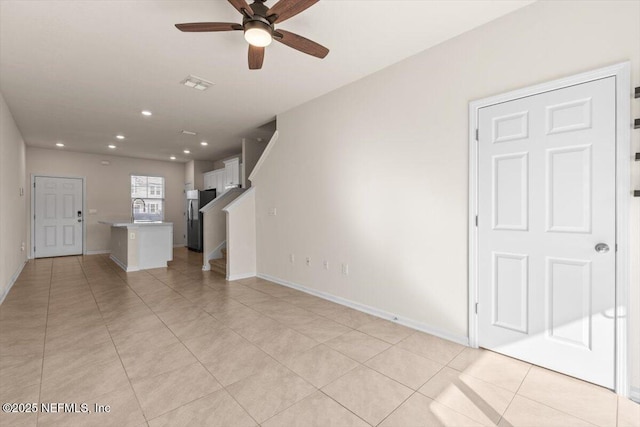 unfurnished living room with light tile patterned floors, visible vents, ceiling fan, stairway, and a sink