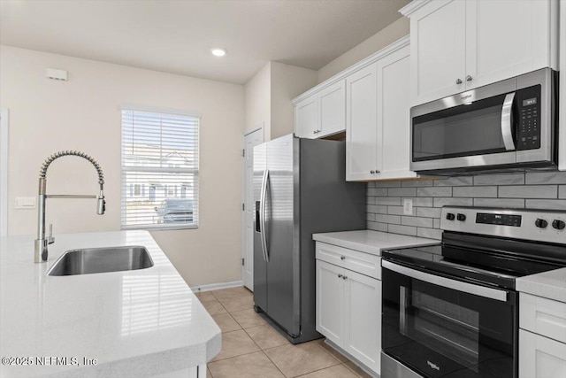 kitchen featuring white cabinets, a sink, stainless steel appliances, light countertops, and backsplash