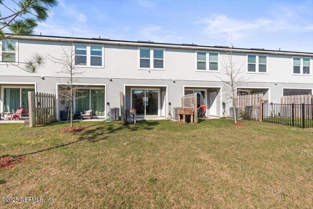 rear view of house with a yard, fence, and stucco siding