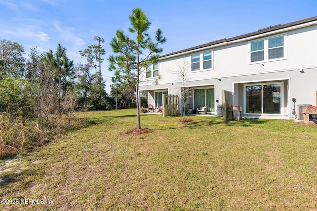 rear view of house with central air condition unit, a lawn, and stucco siding