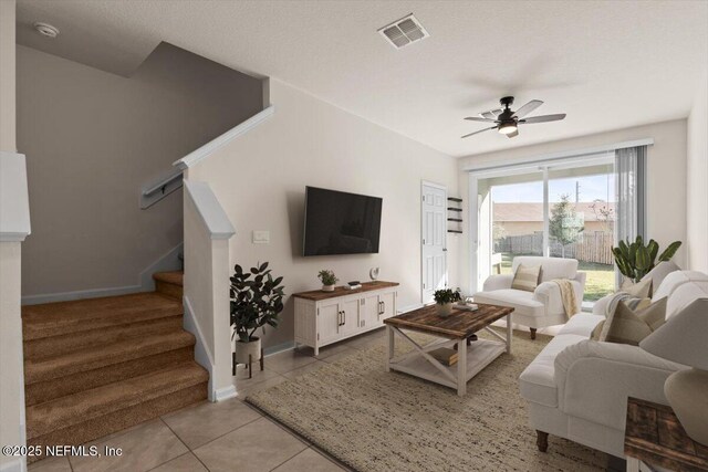 living room with light tile patterned floors, visible vents, stairway, ceiling fan, and baseboards