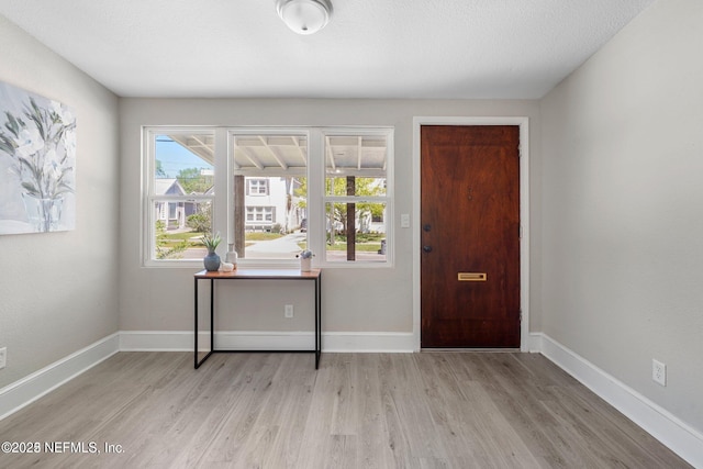 foyer featuring a textured ceiling, light wood finished floors, and baseboards