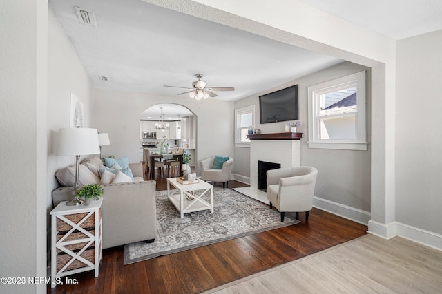 living room featuring arched walkways, visible vents, a brick fireplace, wood finished floors, and baseboards