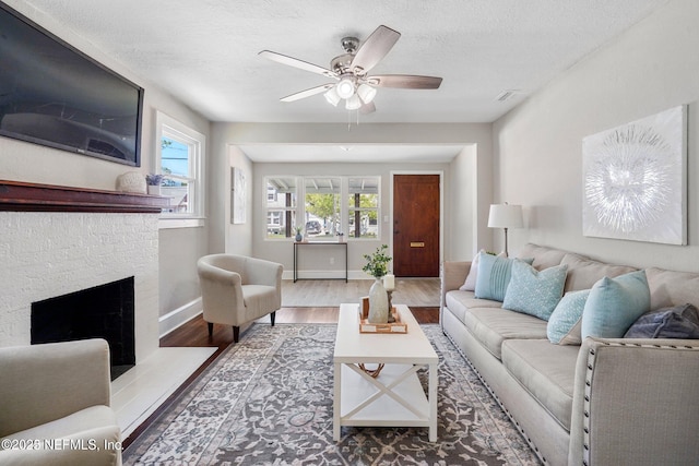 living area with a textured ceiling, a brick fireplace, wood finished floors, and baseboards