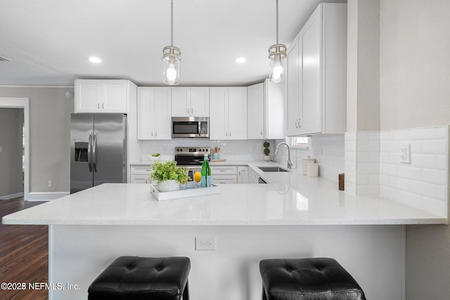 kitchen featuring dark wood finished floors, stainless steel appliances, backsplash, a sink, and a peninsula