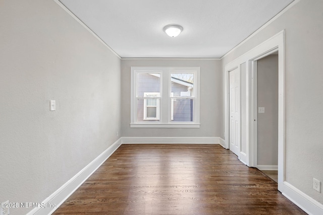 spare room featuring ornamental molding, dark wood-type flooring, and baseboards