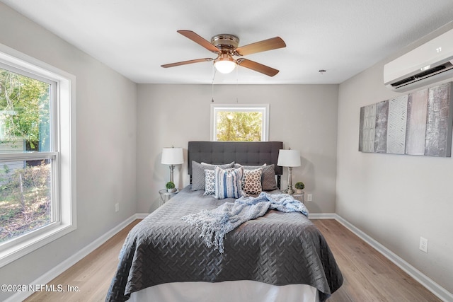 bedroom with baseboards, ceiling fan, a wall unit AC, and light wood-style floors