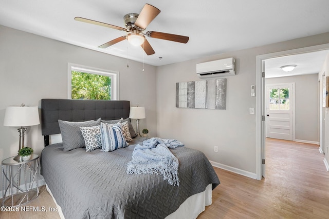 bedroom with ceiling fan, baseboards, an AC wall unit, and wood finished floors