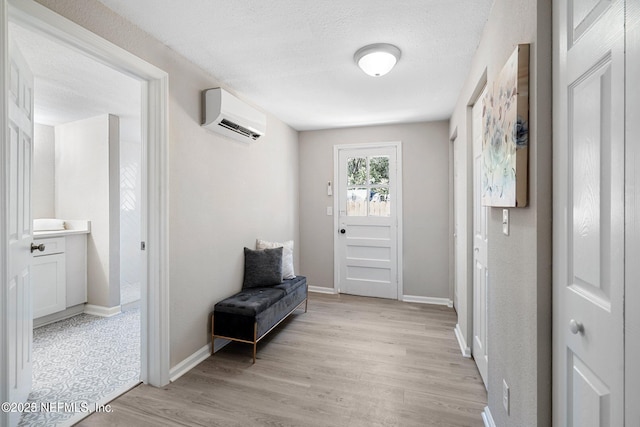 foyer with baseboards, a wall unit AC, light wood-style flooring, and a textured ceiling