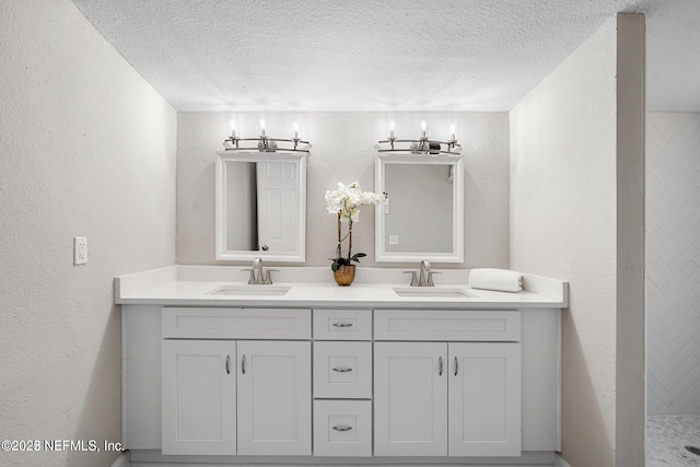 bathroom featuring a textured wall, a sink, a textured ceiling, and double vanity