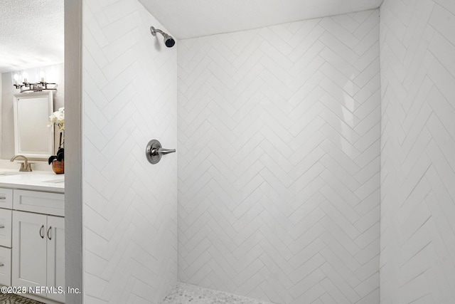 bathroom with a textured ceiling, a tile shower, and vanity