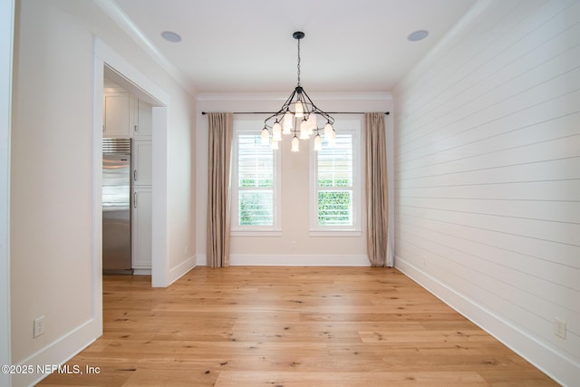 unfurnished dining area featuring light wood-style floors, a notable chandelier, ornamental molding, and baseboards