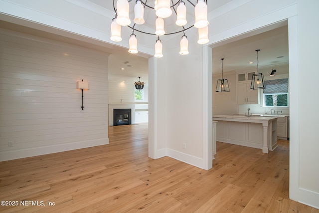 unfurnished dining area with baseboards, a fireplace, an inviting chandelier, and light wood-style floors