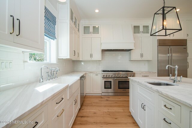 kitchen with premium range hood, high quality appliances, white cabinets, and a sink