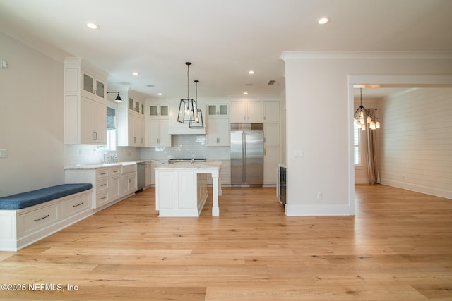 kitchen with decorative backsplash, an island with sink, stainless steel appliances, light wood-style floors, and white cabinetry