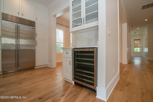 kitchen with wine cooler, built in refrigerator, visible vents, light wood-type flooring, and decorative backsplash