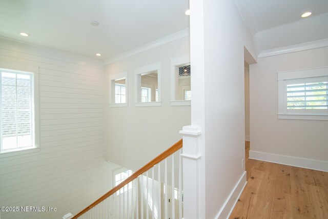 corridor featuring light wood-type flooring, baseboards, ornamental molding, and an upstairs landing