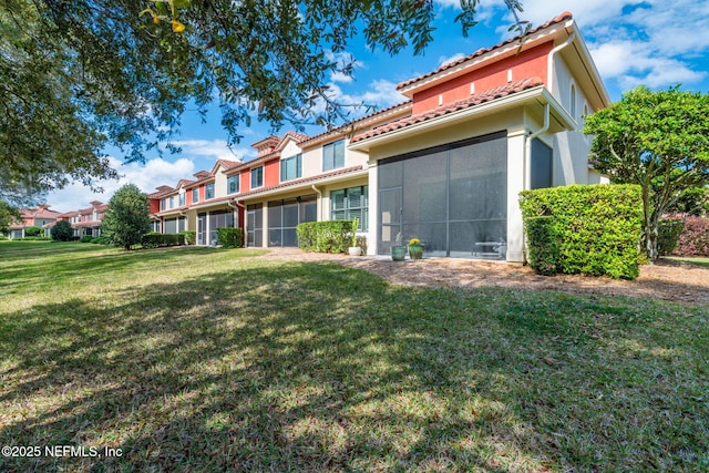 back of property featuring stucco siding, a tiled roof, a yard, and a sunroom