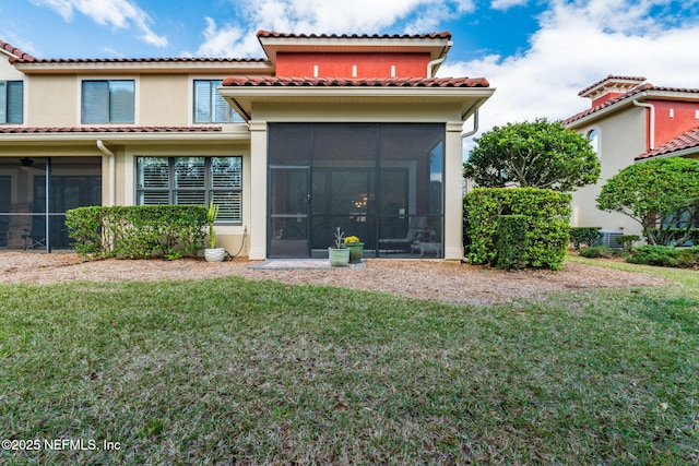 rear view of house featuring a tiled roof, stucco siding, a lawn, and a sunroom