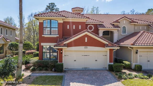 mediterranean / spanish-style house with stucco siding, a tile roof, and decorative driveway