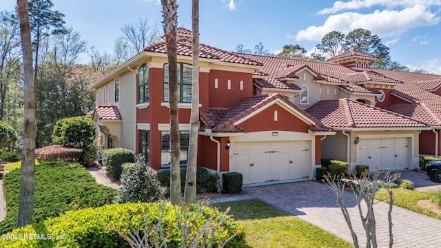 mediterranean / spanish home with stucco siding, a tile roof, decorative driveway, and a garage