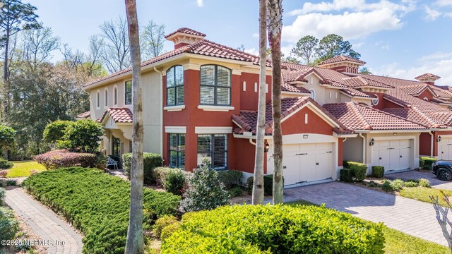 mediterranean / spanish-style home with a tiled roof, decorative driveway, an attached garage, and stucco siding