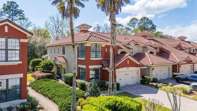 mediterranean / spanish home featuring a residential view, a tiled roof, stucco siding, decorative driveway, and an attached garage