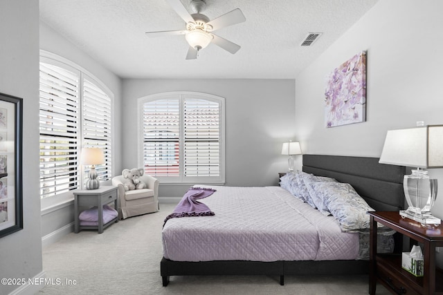 bedroom with visible vents, a textured ceiling, carpet floors, baseboards, and ceiling fan