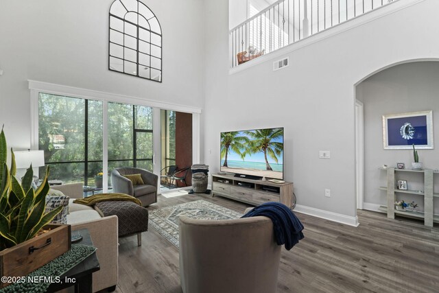 living area featuring visible vents, wood finished floors, arched walkways, baseboards, and a towering ceiling