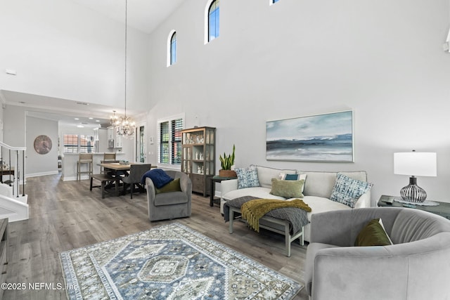 living room featuring a notable chandelier, light wood-style flooring, stairs, and baseboards