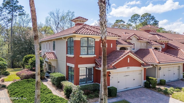 mediterranean / spanish-style house with stucco siding, a tiled roof, decorative driveway, and a garage