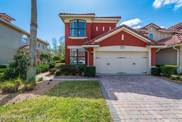 mediterranean / spanish home with decorative driveway, a garage, stucco siding, and a tiled roof