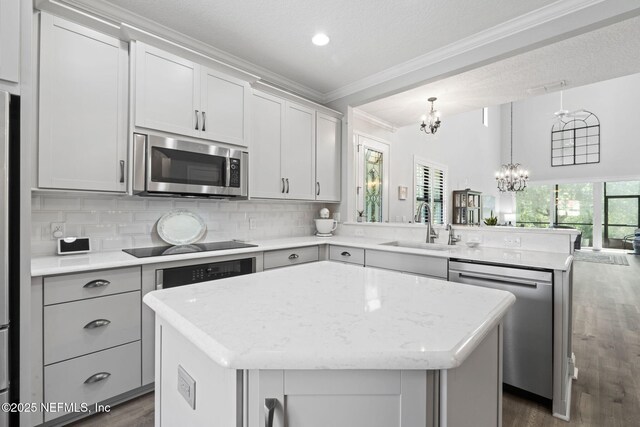 kitchen featuring a peninsula, a sink, appliances with stainless steel finishes, a chandelier, and a center island