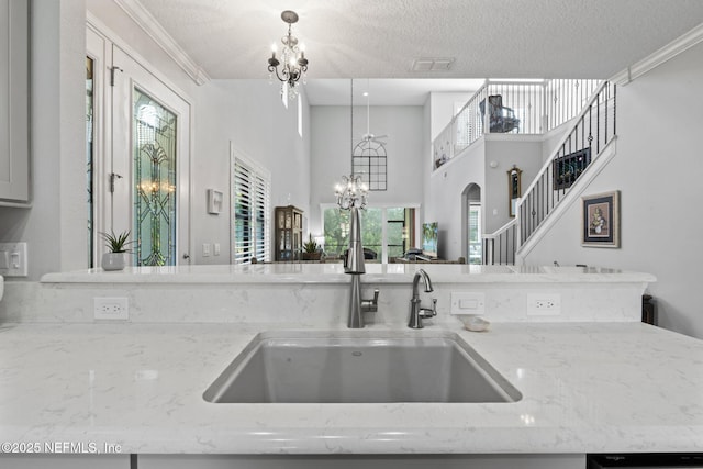 kitchen featuring light stone counters, a textured ceiling, a chandelier, and a sink