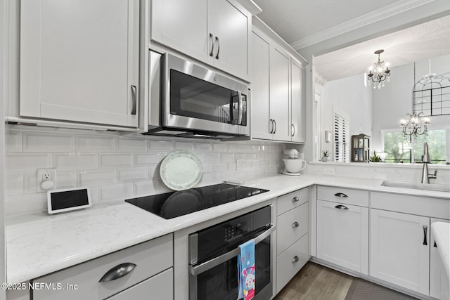 kitchen featuring crown molding, decorative backsplash, appliances with stainless steel finishes, an inviting chandelier, and a sink