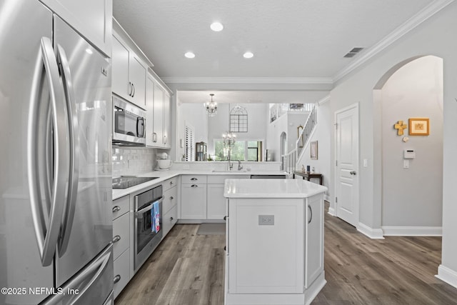 kitchen featuring visible vents, a kitchen island, ornamental molding, appliances with stainless steel finishes, and arched walkways