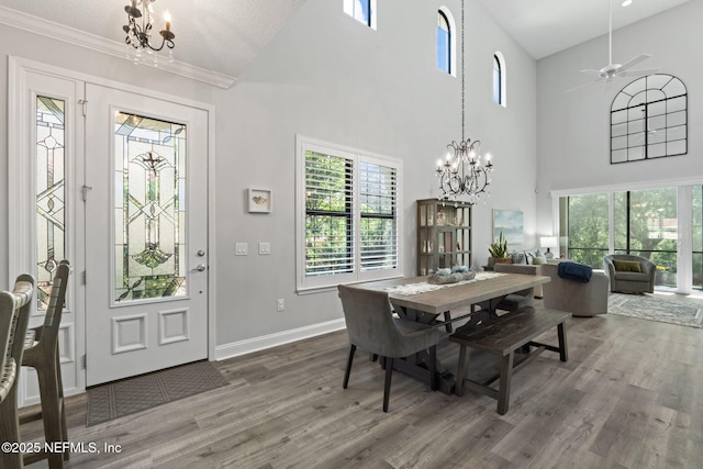 dining area with ceiling fan with notable chandelier, a high ceiling, wood finished floors, and baseboards