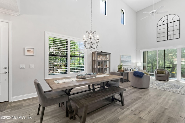 dining space featuring ceiling fan with notable chandelier, a high ceiling, baseboards, and wood finished floors