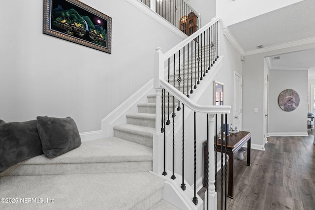 staircase featuring visible vents, crown molding, baseboards, and wood finished floors