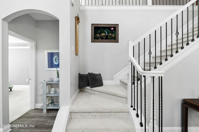 staircase with arched walkways, baseboards, and wood finished floors