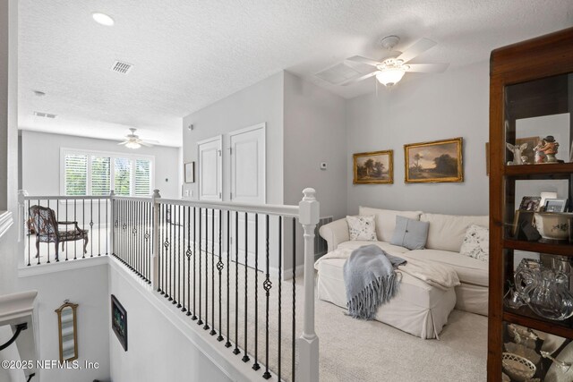 hall with an upstairs landing, visible vents, a textured ceiling, and carpet floors