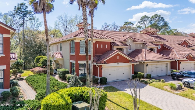 mediterranean / spanish-style house with a front yard, stucco siding, a garage, a tile roof, and decorative driveway